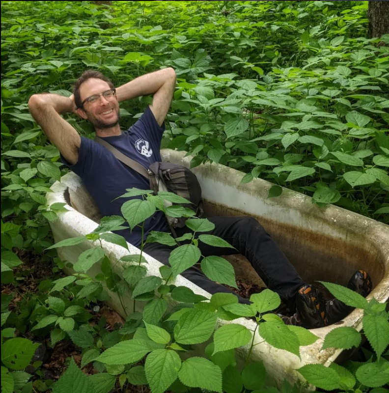 This is a photo of Caleb in a bathtub, which is in the middle of a forest.